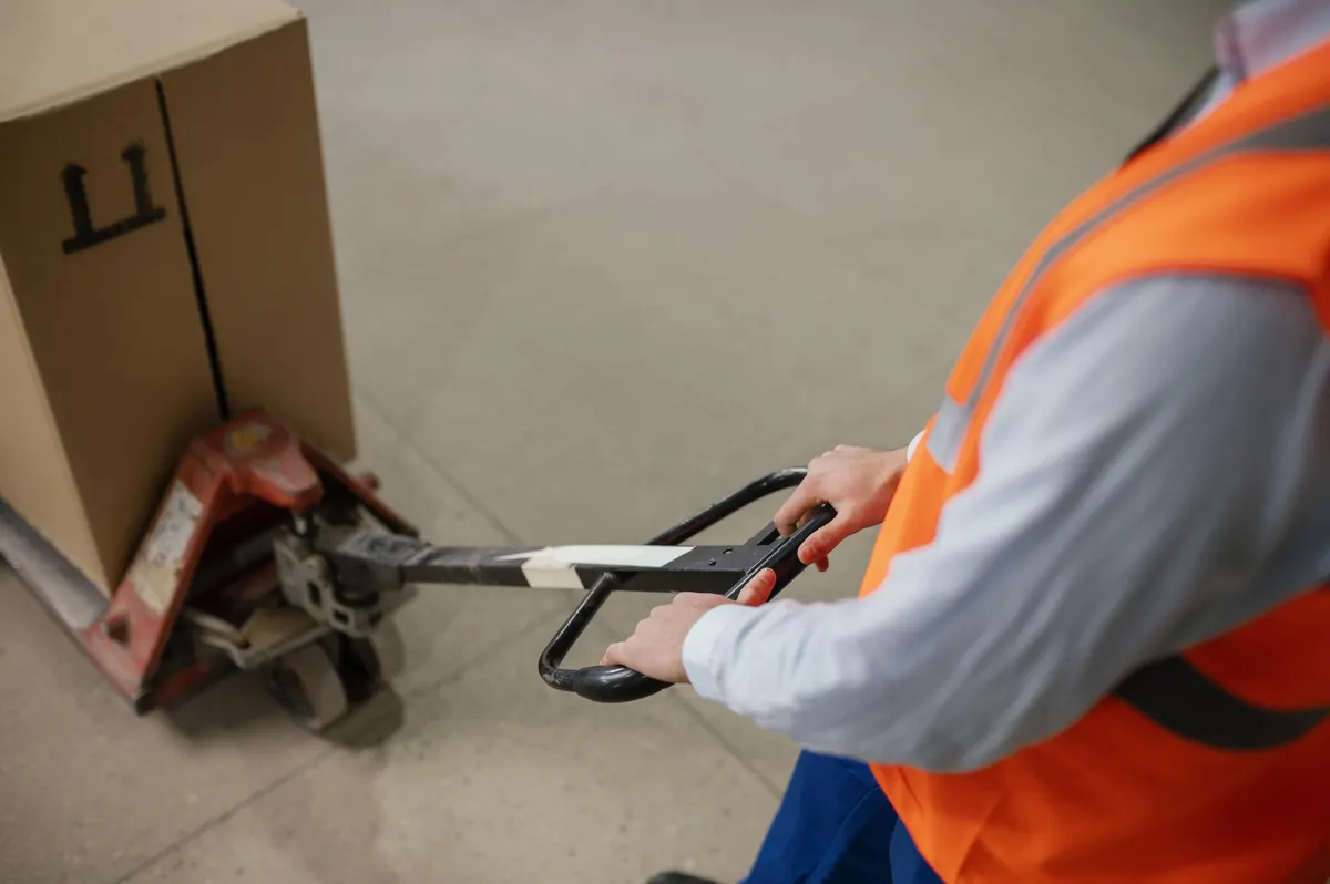 Mitarbeiter mit Warnweste bewegt Ware mit dem Hubwagen
